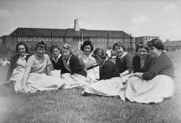 9 female students sitting on the school field in 1950s from the East Barnet School history archive.