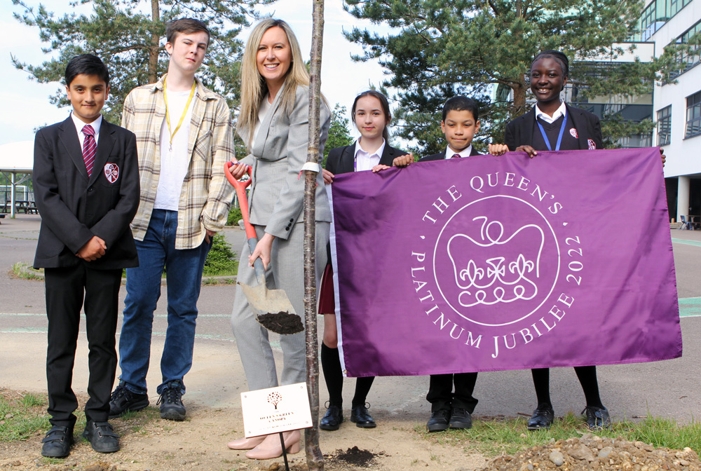 A selection of students and the Headteacher planting a tree for the The Queen's Green Canopy. The students are holding a purple Queen's Platinum Jubilee flag.