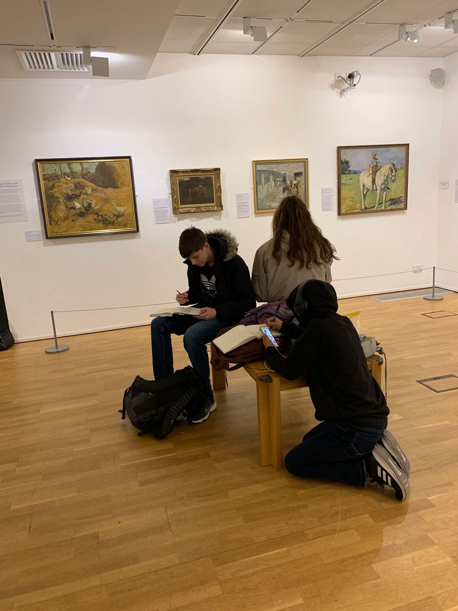students sitting in the middle of an art gallery drawing