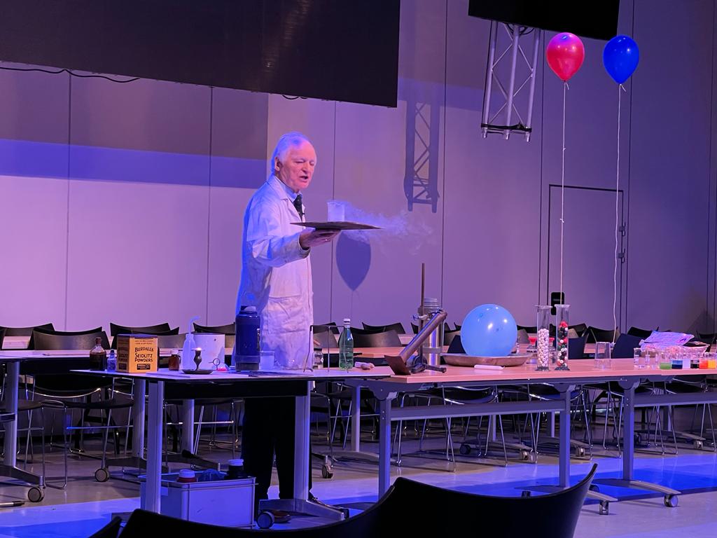 A chemistry teacher in a lab coat holding a tray with a beaker
