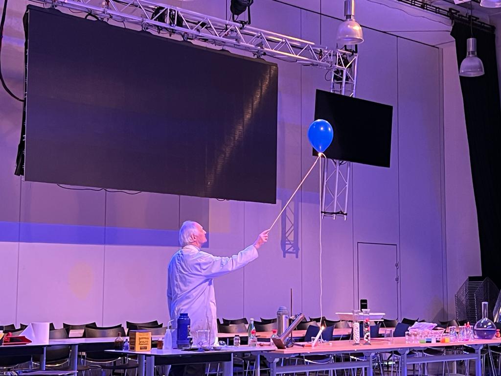 A chemistry teacher in a lab coat holding on to a balloon that is flying away