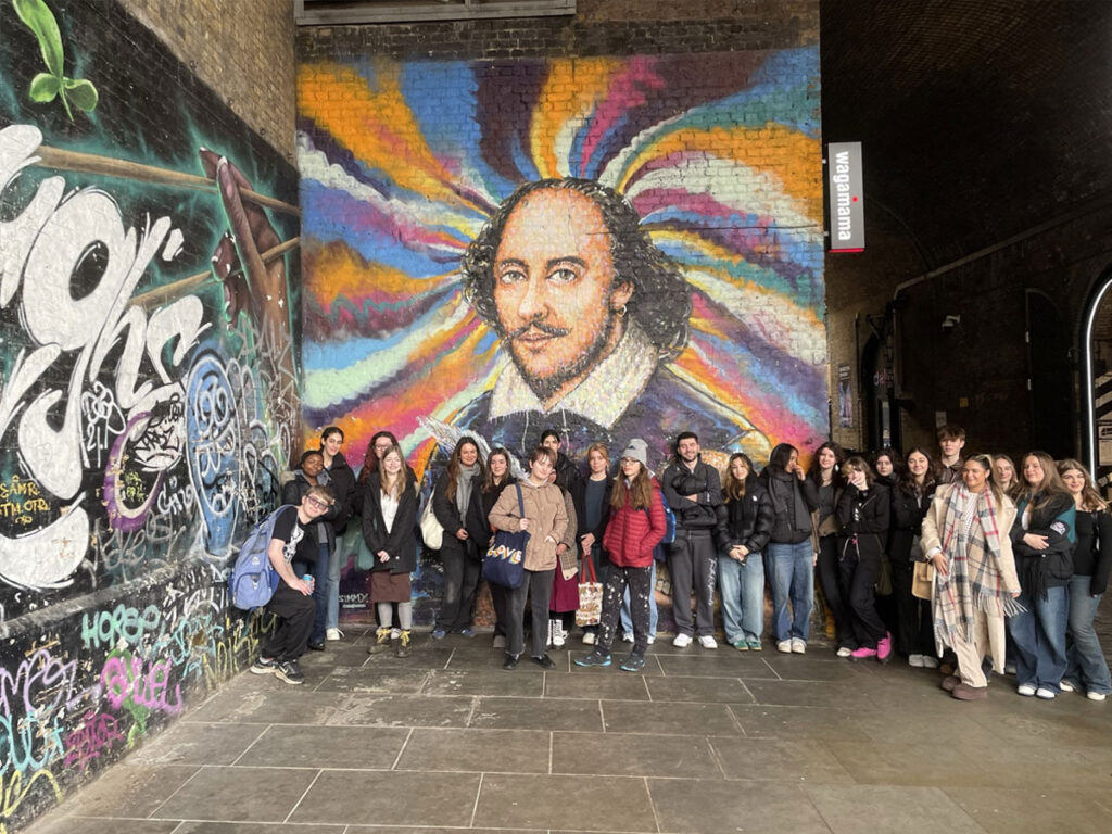 students stood in front of a large wall mural of William Shakespeare