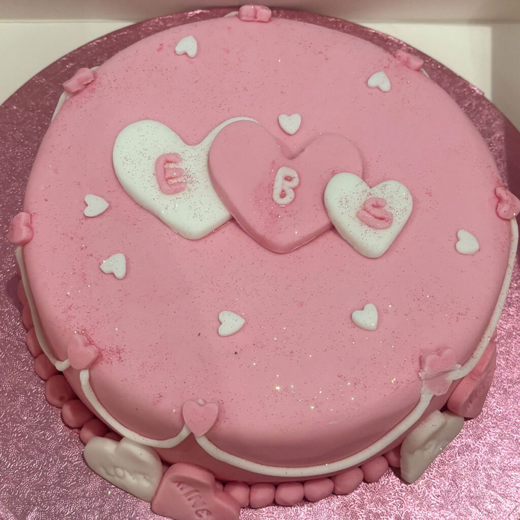 a pink round cake with three hearts in the middle with ebs written