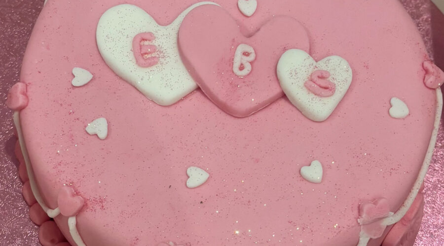 a pink round cake with three hearts in the middle with ebs written