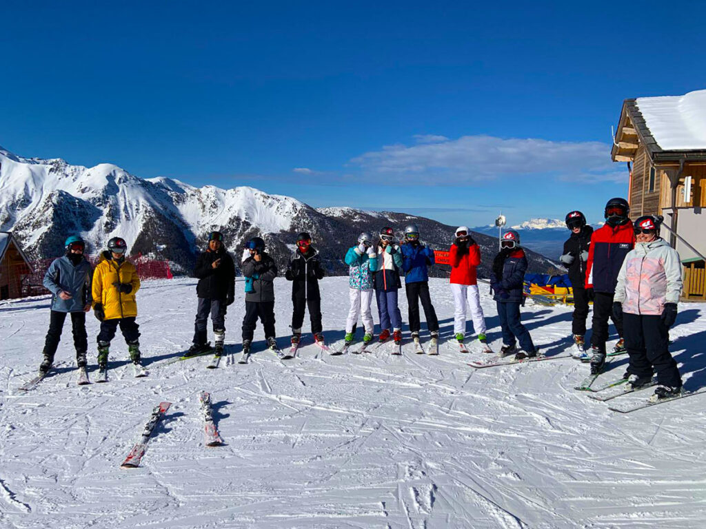 students stop their ski to pose in a line at the top of the slope